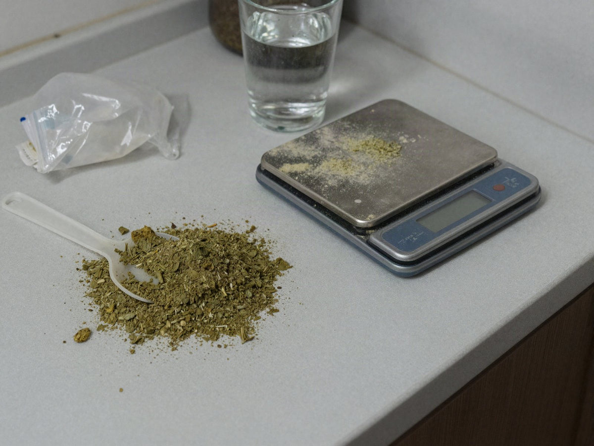 Loose kratom powder spilled on a kitchen counter beside a plastic scoop and a dusty scale