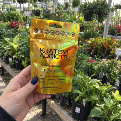 A hand holding Monster Mango kratom gummies in a garden center