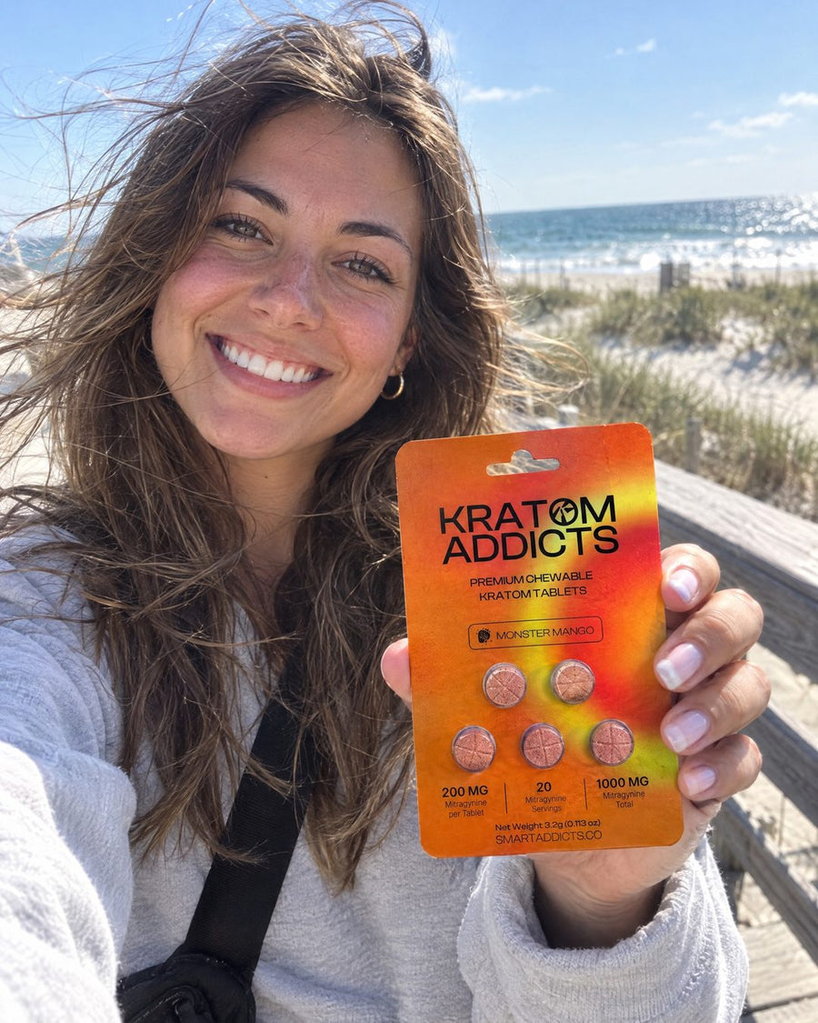 A smiling woman on the beach holding Monster Mango kratom tablets