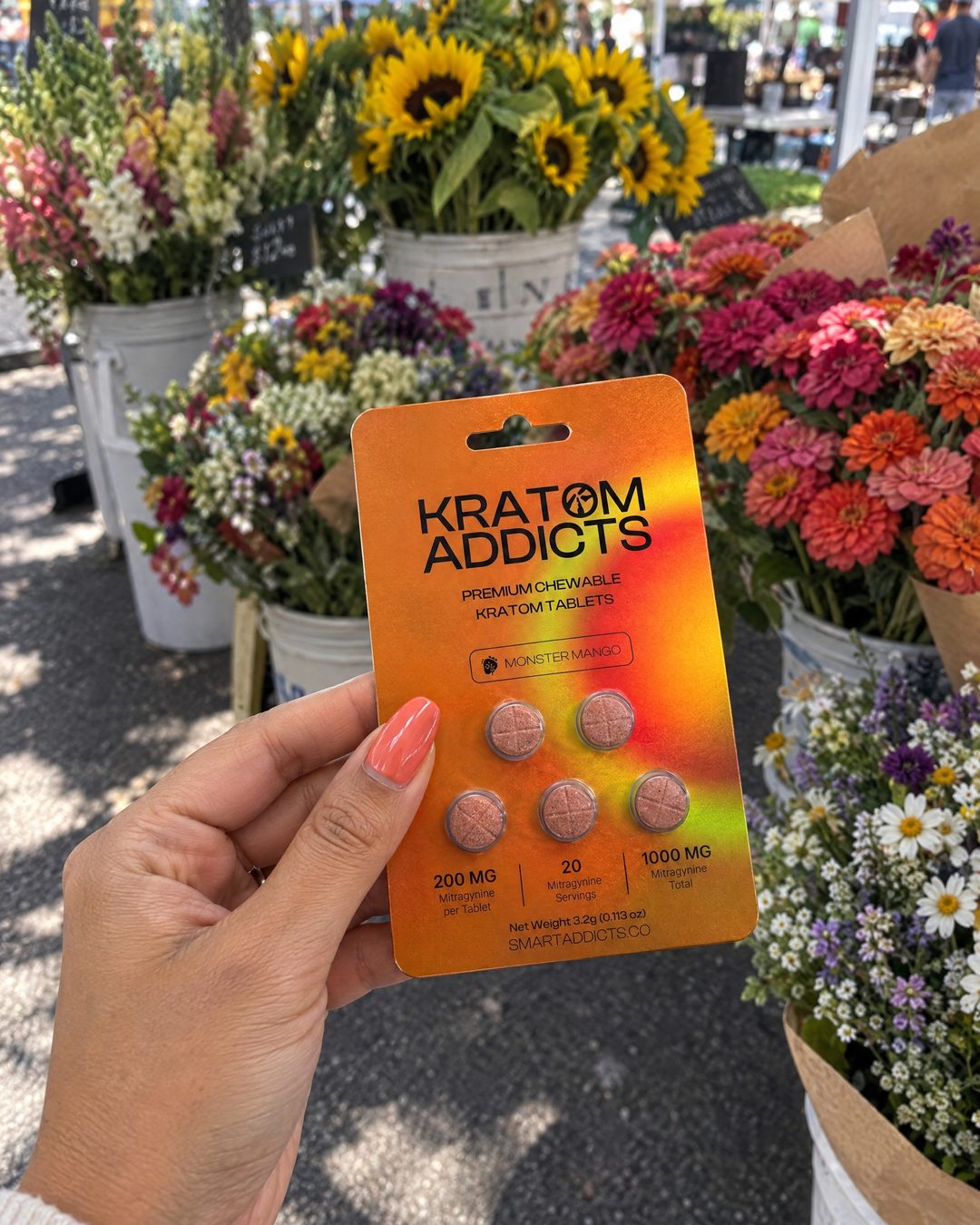 A hand holding Monster Mango kratom tablets at a flower market