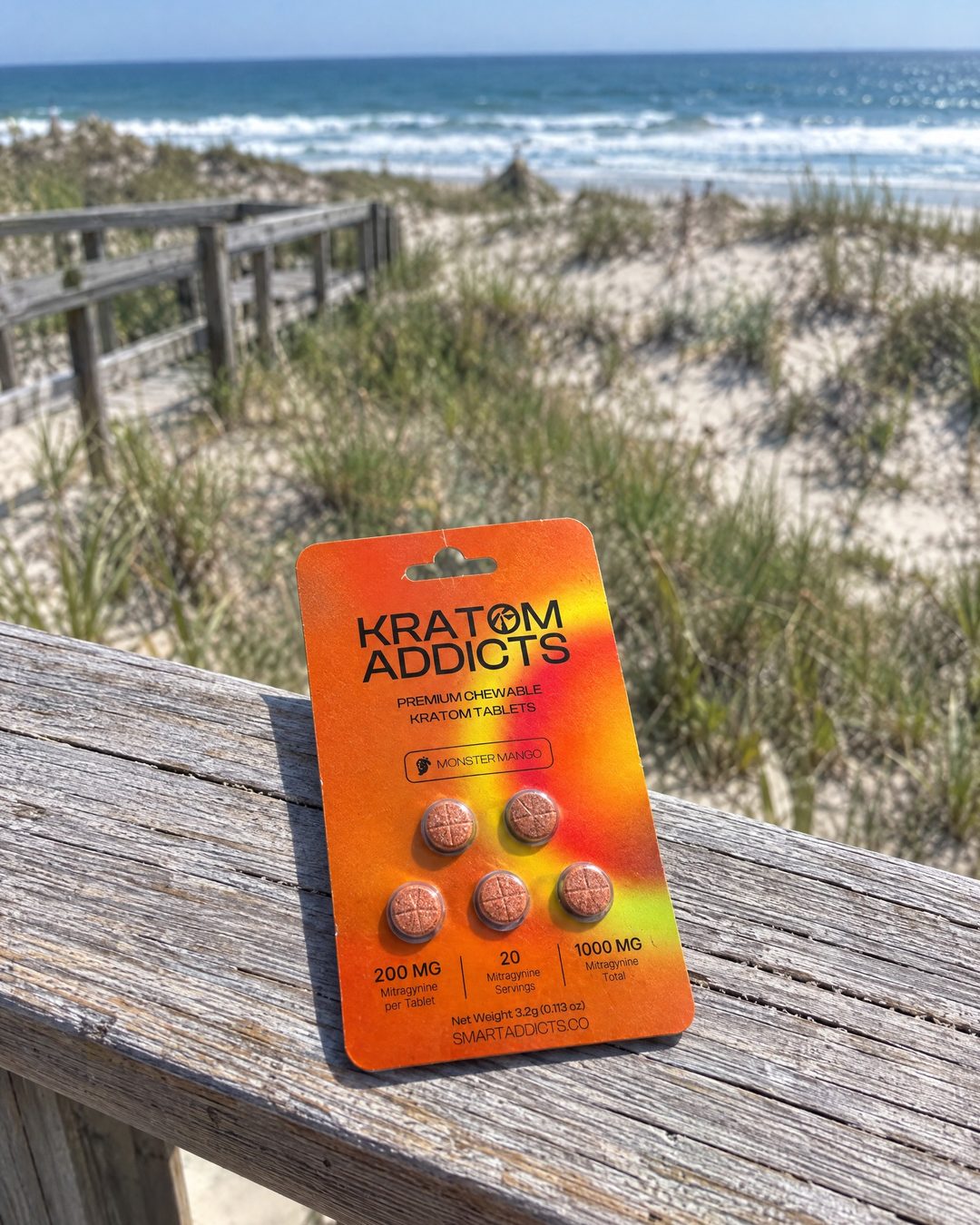 Monster Mango kratom tablets on a boardwalk rail above the beach