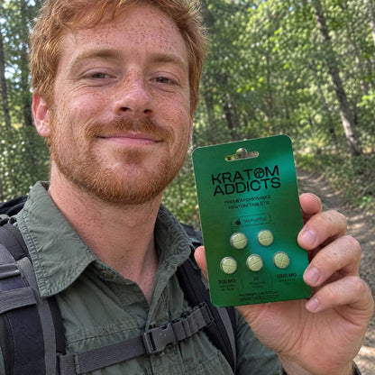 A man on a forest trail holding Sour Apple kratom tablets