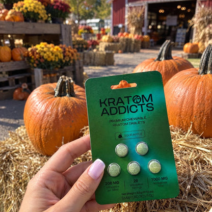 A hand holding Sour Apple kratom tablets at an autumn farm stand