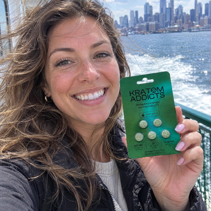 A woman on a ferry with the city behind her, holding Sour Apple kratom tablets