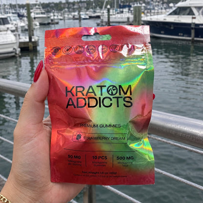 A hand holding Strawberry Dream kratom gummies at a marina