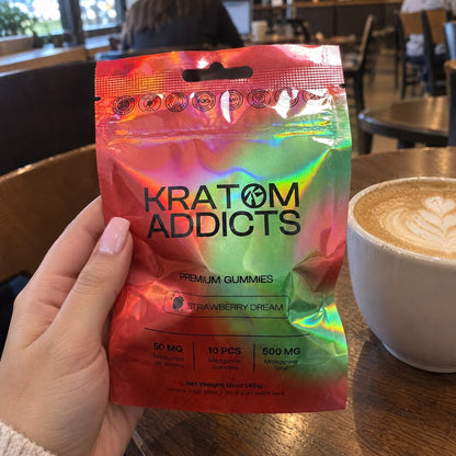 A hand holding Strawberry Dream kratom gummies in a café, a latte on the table