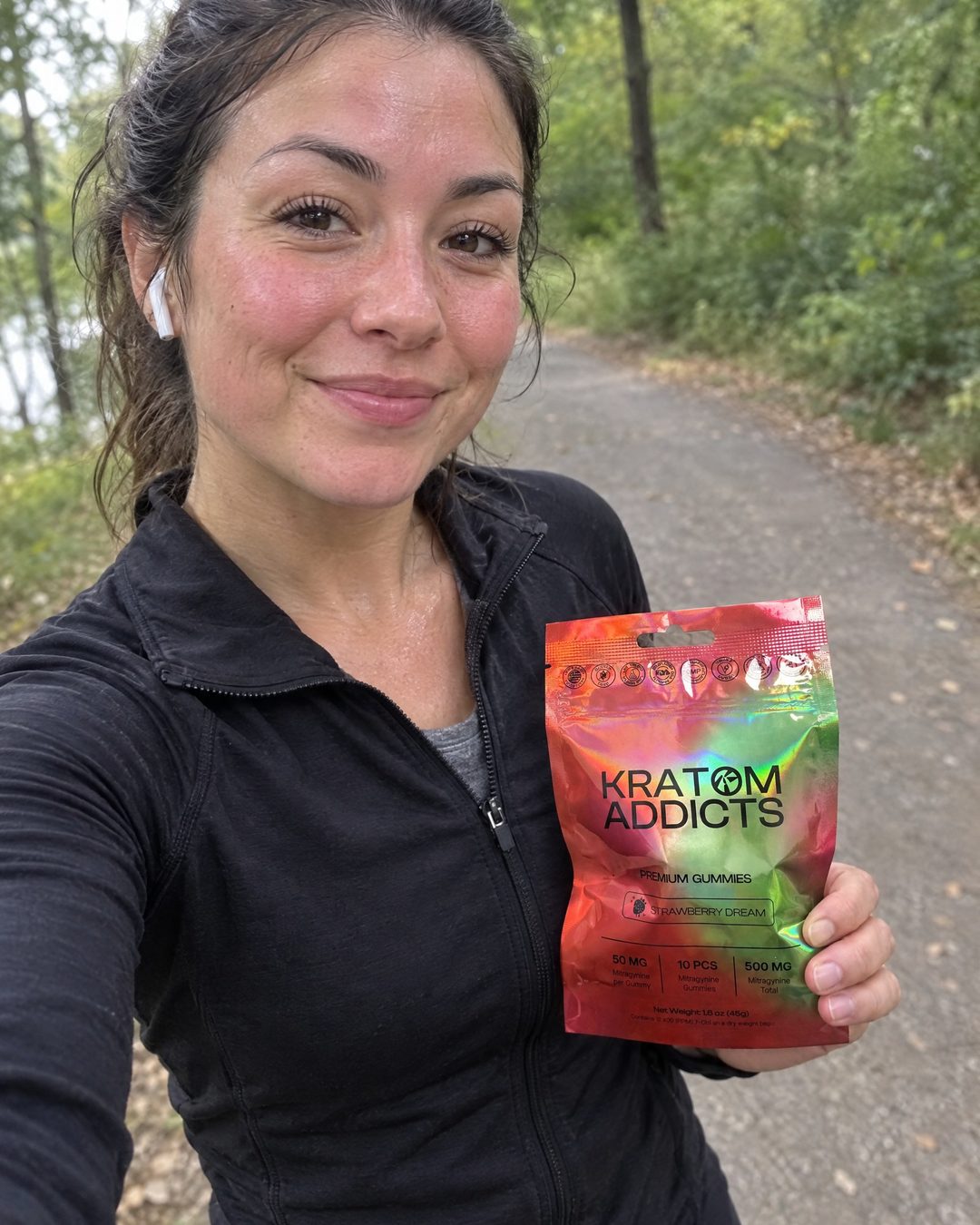 A smiling woman on a park trail holding Strawberry Dream kratom gummies