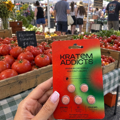 A hand holding Strawberry Dream kratom tablets at a farmers market