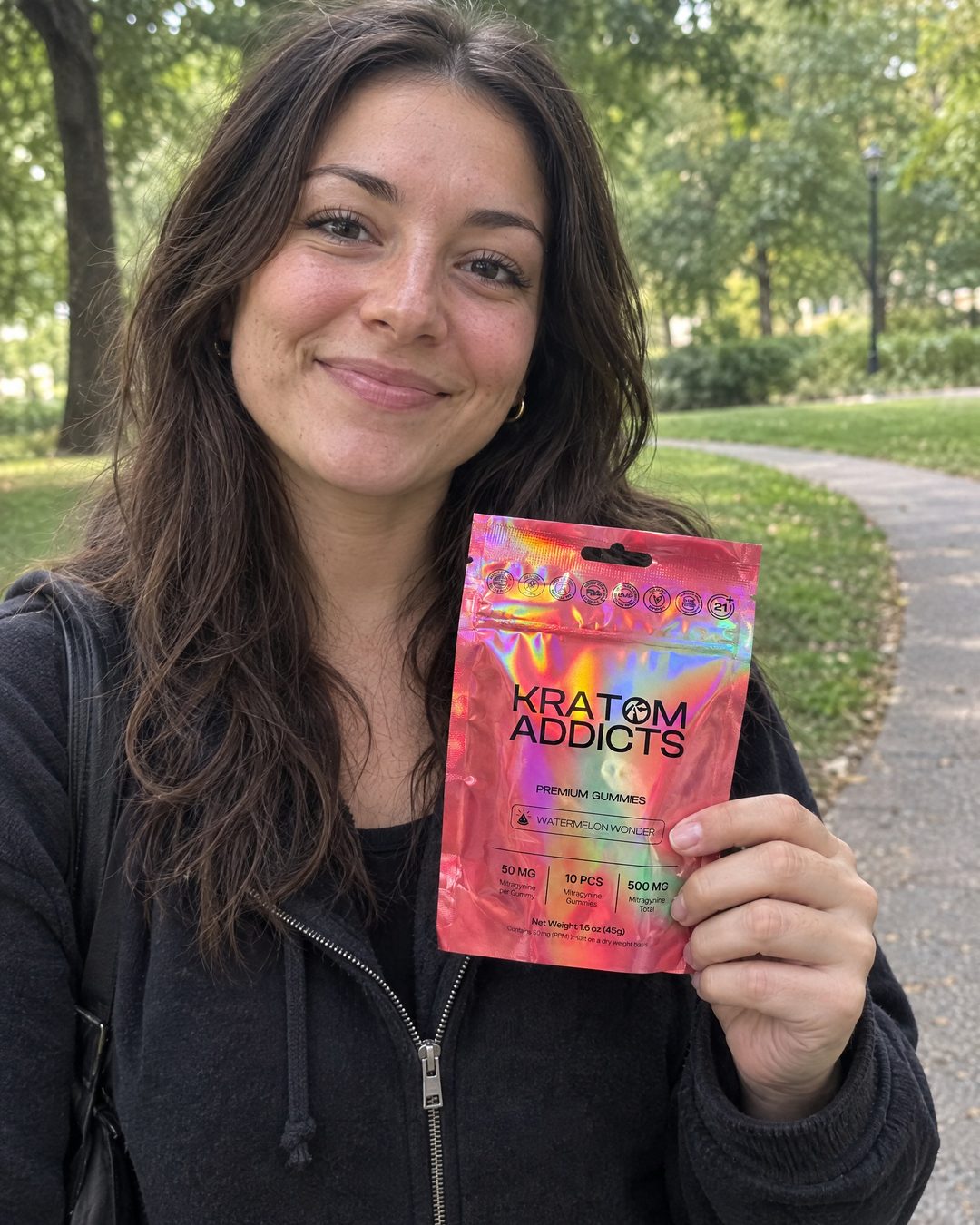 A smiling woman in a park holding Watermelon Wonder kratom gummies