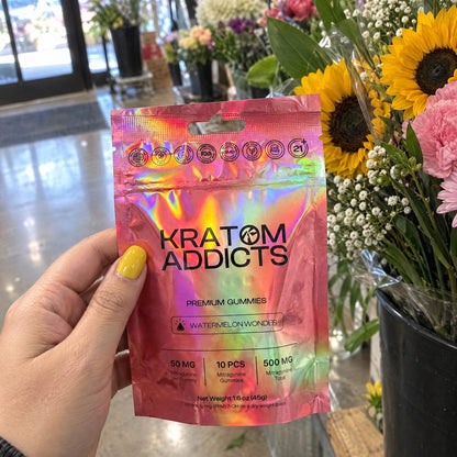 A hand holding Watermelon Wonder kratom gummies by a flower stall