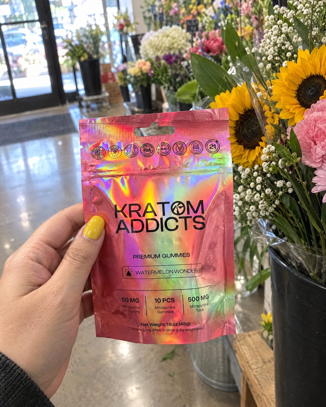A hand holding Watermelon Wonder kratom gummies by a flower stall