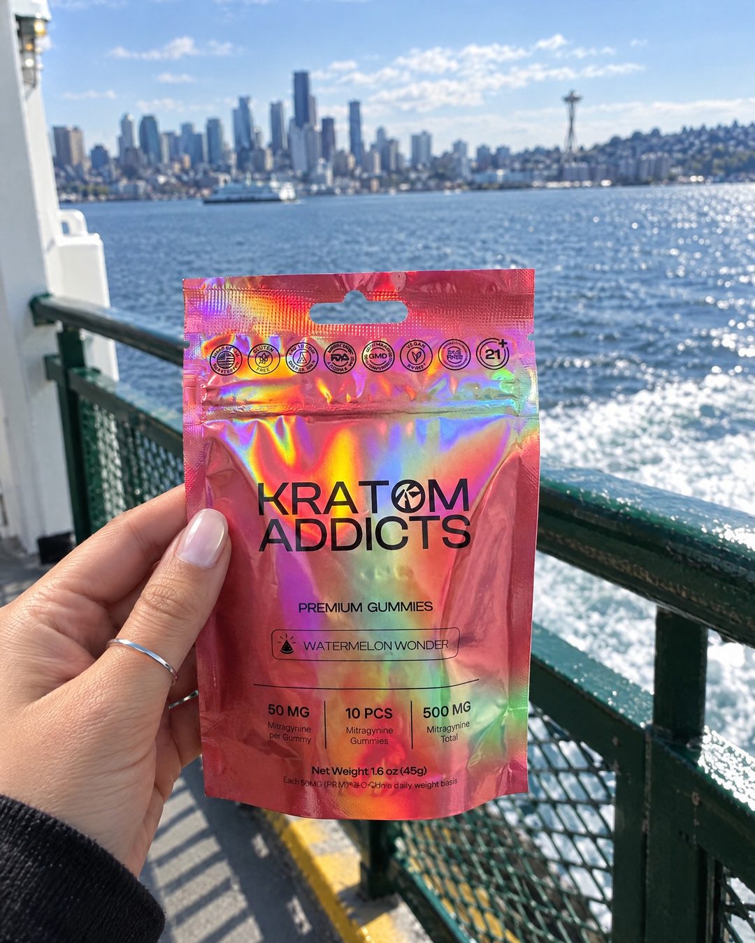 A hand holding Watermelon Wonder kratom gummies on a ferry, the city skyline behind