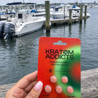A hand holding Watermelon Wonder kratom tablets at a marina