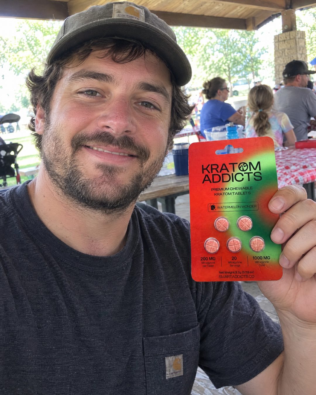 A man at an outdoor table holding Watermelon Wonder kratom tablets