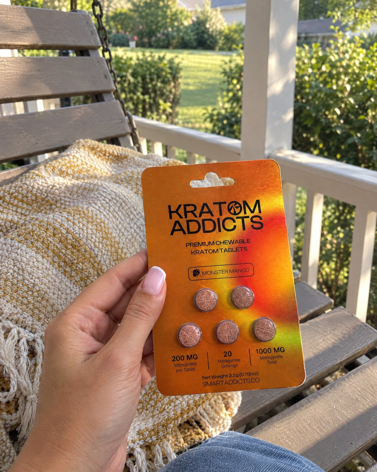 A hand holding Monster Mango kratom tablets on a porch swing