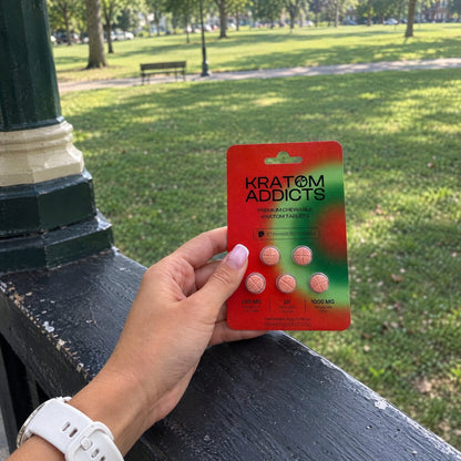 A hand holding Strawberry Dream kratom tablets in a park