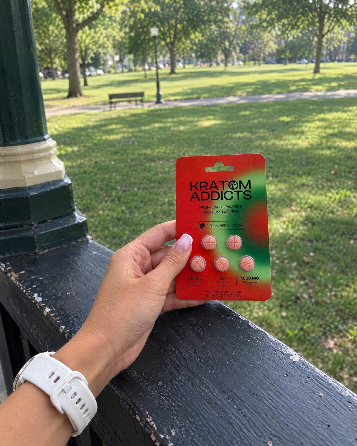 A hand holding Strawberry Dream kratom tablets in a park