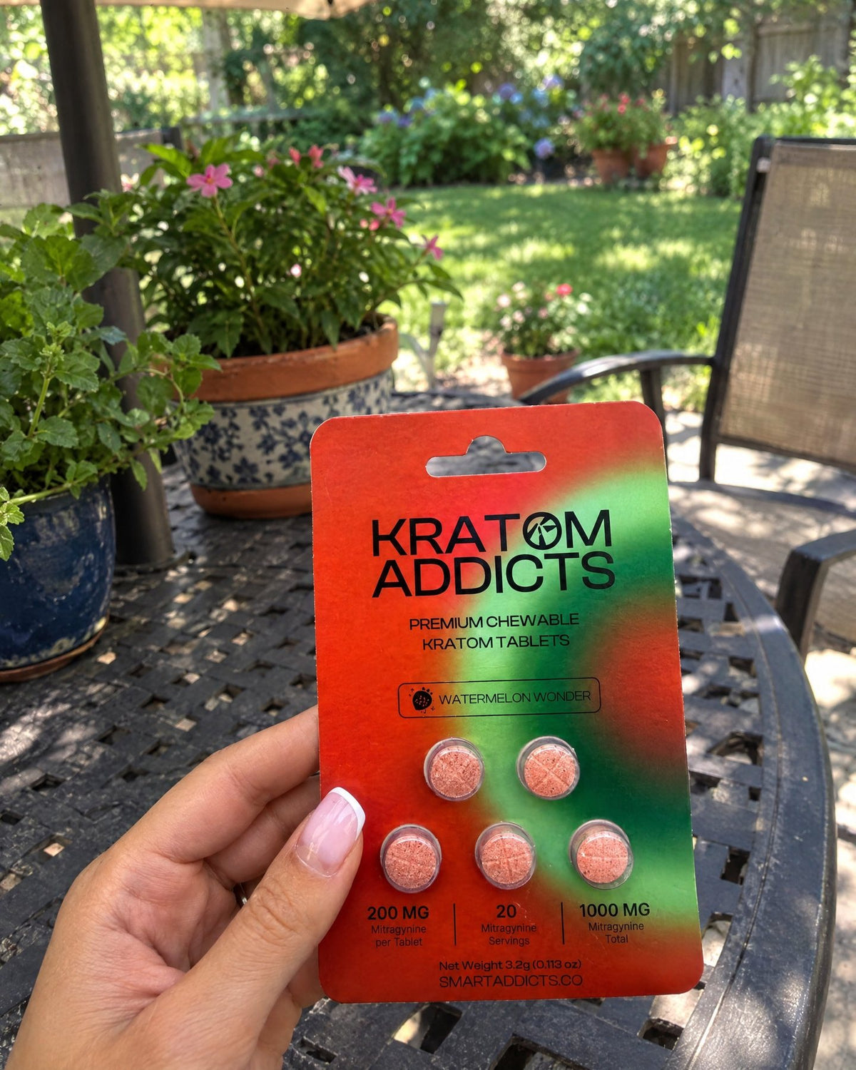 A hand holding Watermelon Wonder kratom tablets on a garden patio